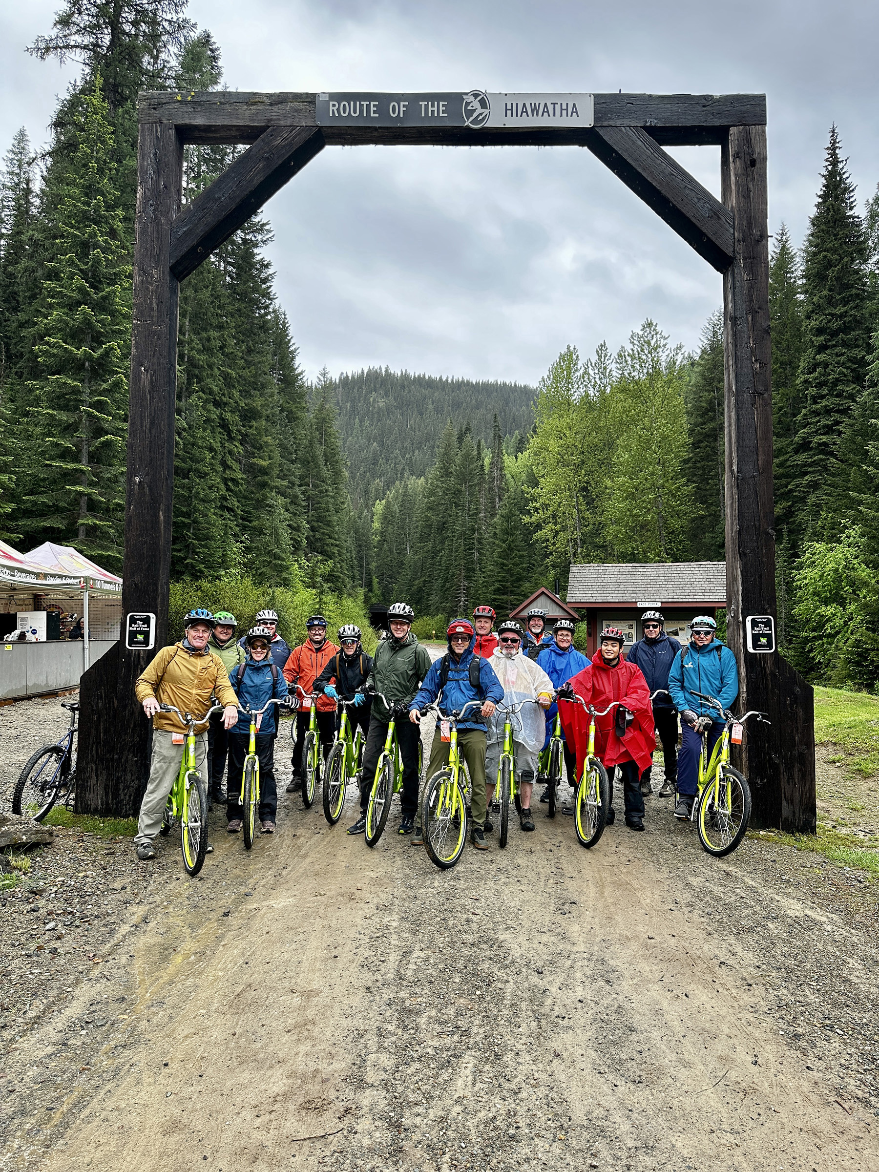 Group adults with bright yellow bikes standing under the Route of the Hiawatha entrance arch, highlighting Idaho’s summer recreation opportunities