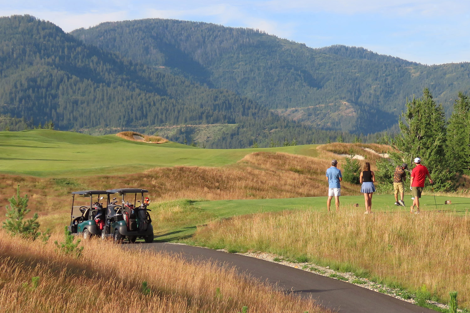 Golfers play a round at Silver Mountain’s Galena Ridge Golf Course in Idaho, with golf carts parked nearby and forested mountain slopes rising in the background.